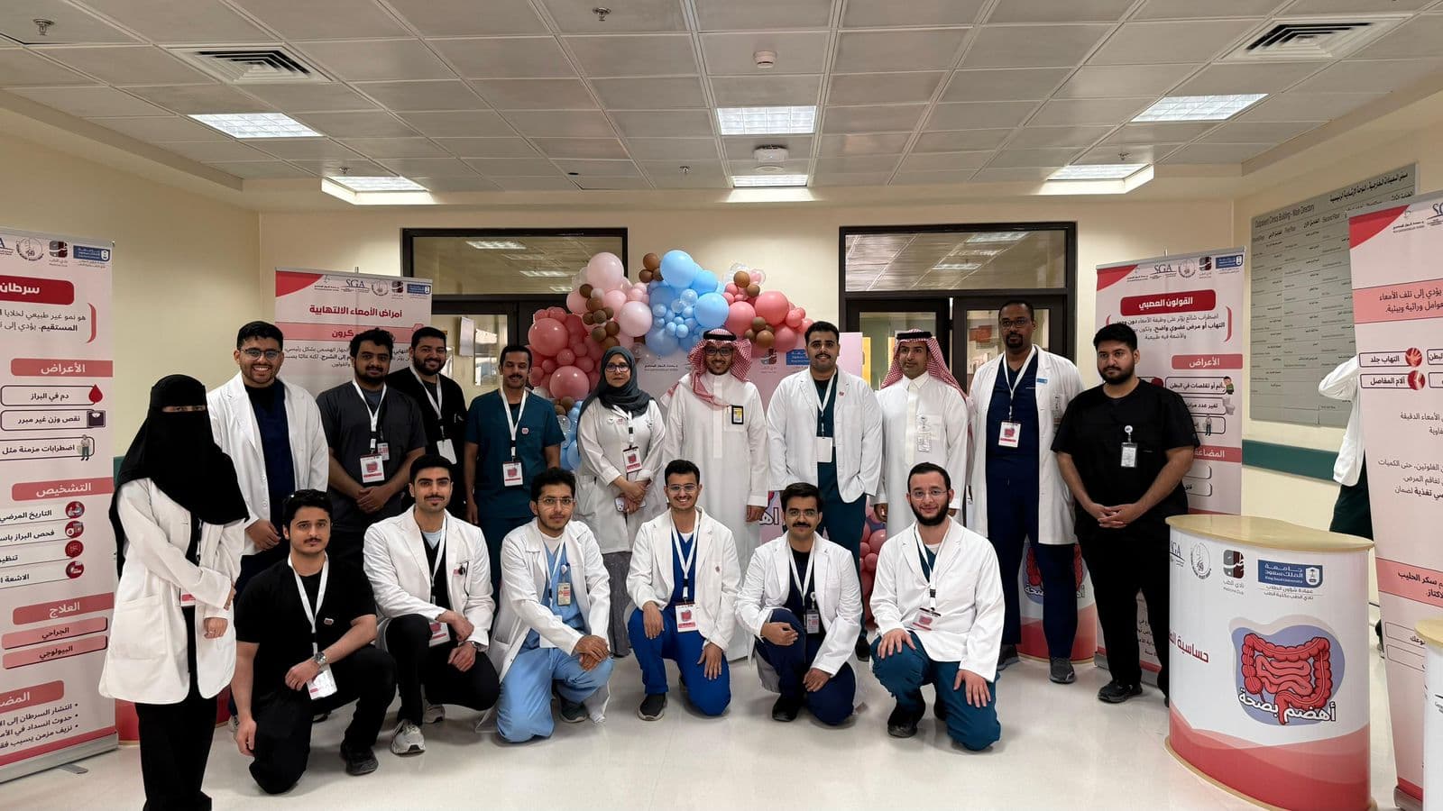 Faculty, residents, and KSU medical students who organised the "Ihdam BiSiha" campaign, pictured at the KKUH outpatient-clinics venue beneath a pink-and-blue balloon arch.