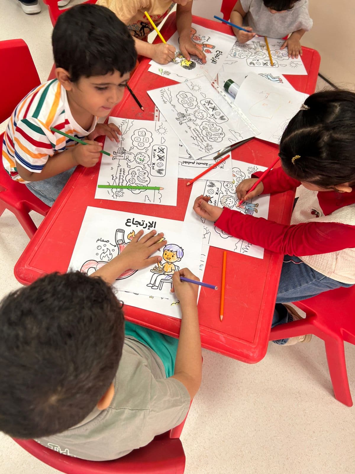 Children at a red activity table colouring educational sheets about gastroesophageal reflux and gut health.
